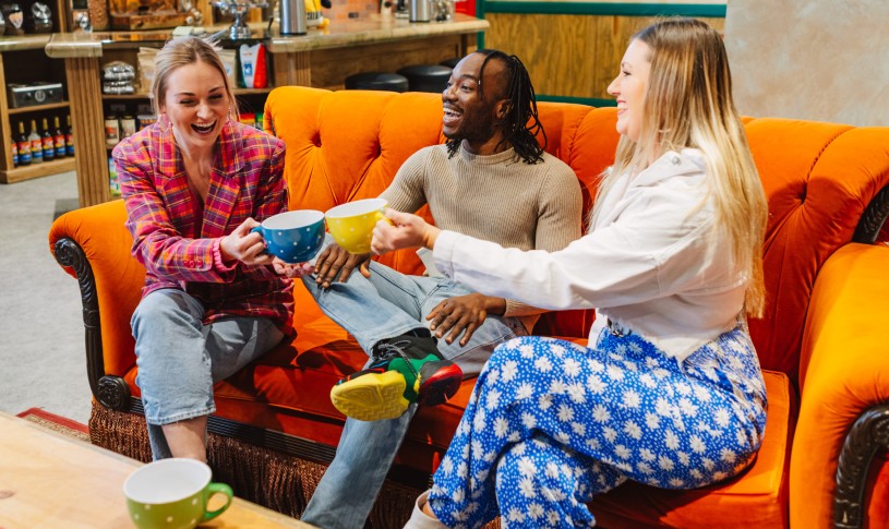 Three friends raising mugs on the couch at Central Perk